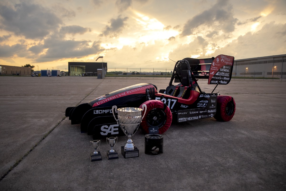 Penn Electric Racing’s REV5 car photographed after the Lincoln FSAE competition, with four trophies in the foreground.