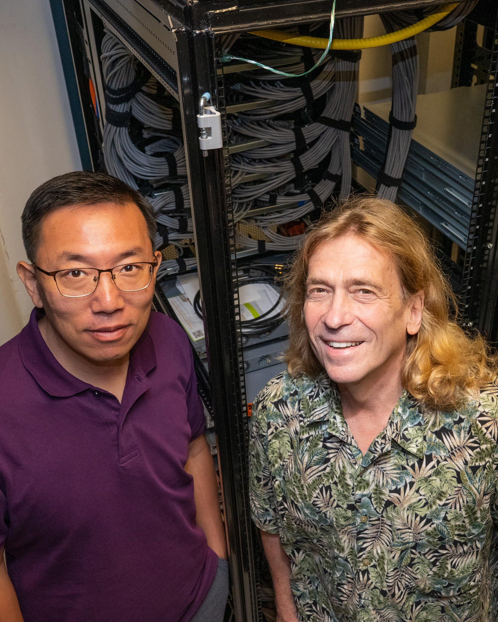 Two researchers stand in front of a server rack full of cables. 