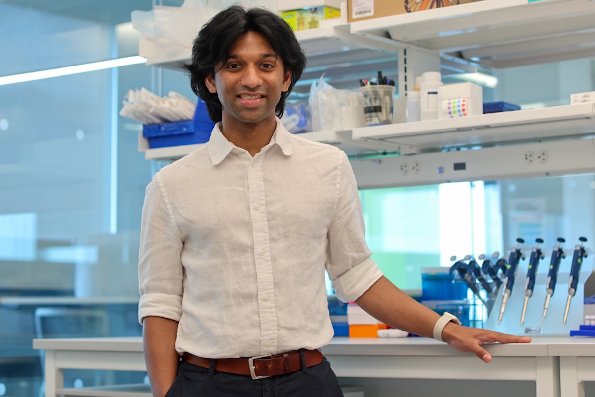 A man in a white dress shirt stands in front of a lab bench. 